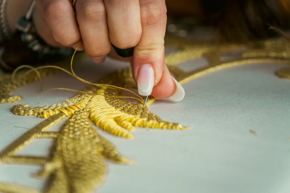 Mani che ricamano una foglia in filato d’oro