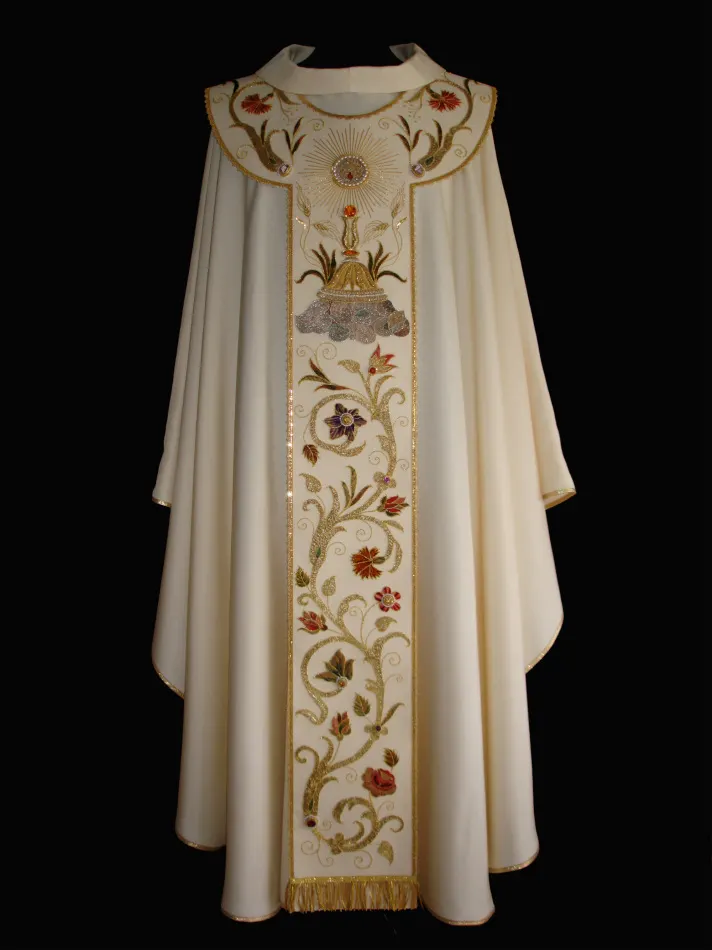 Casula bianca con pallio realizzato su shantung di seta con il riporto di ricami in oro e seta di un antico piviale. Nell'operazione di riporto il ricamo è stato impreziosito da numerose gemme di varia natura e colore, da un prezioso cammeo e da diverse perle.